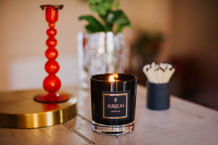 Candle with 'Aureum London' label on a table with decorative items.