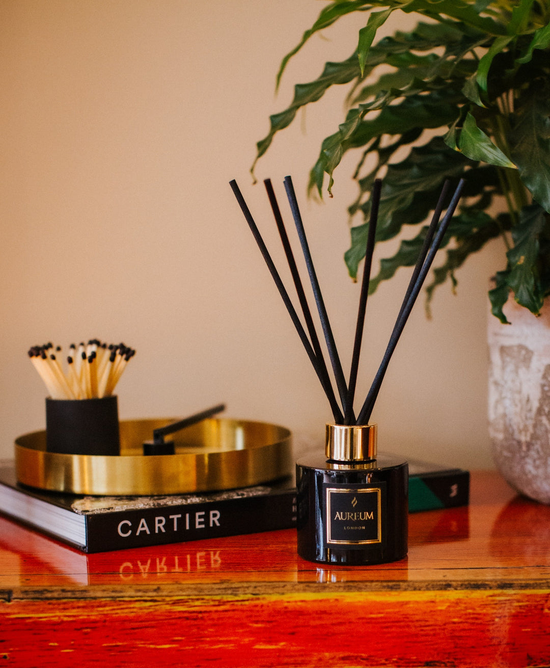 Aromatherapy diffuser with black sticks on a wooden surface with a book and plant in the background.