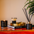 Load image into Gallery viewer, Candle, books, and diffuser on a wooden surface with a plant in the background
