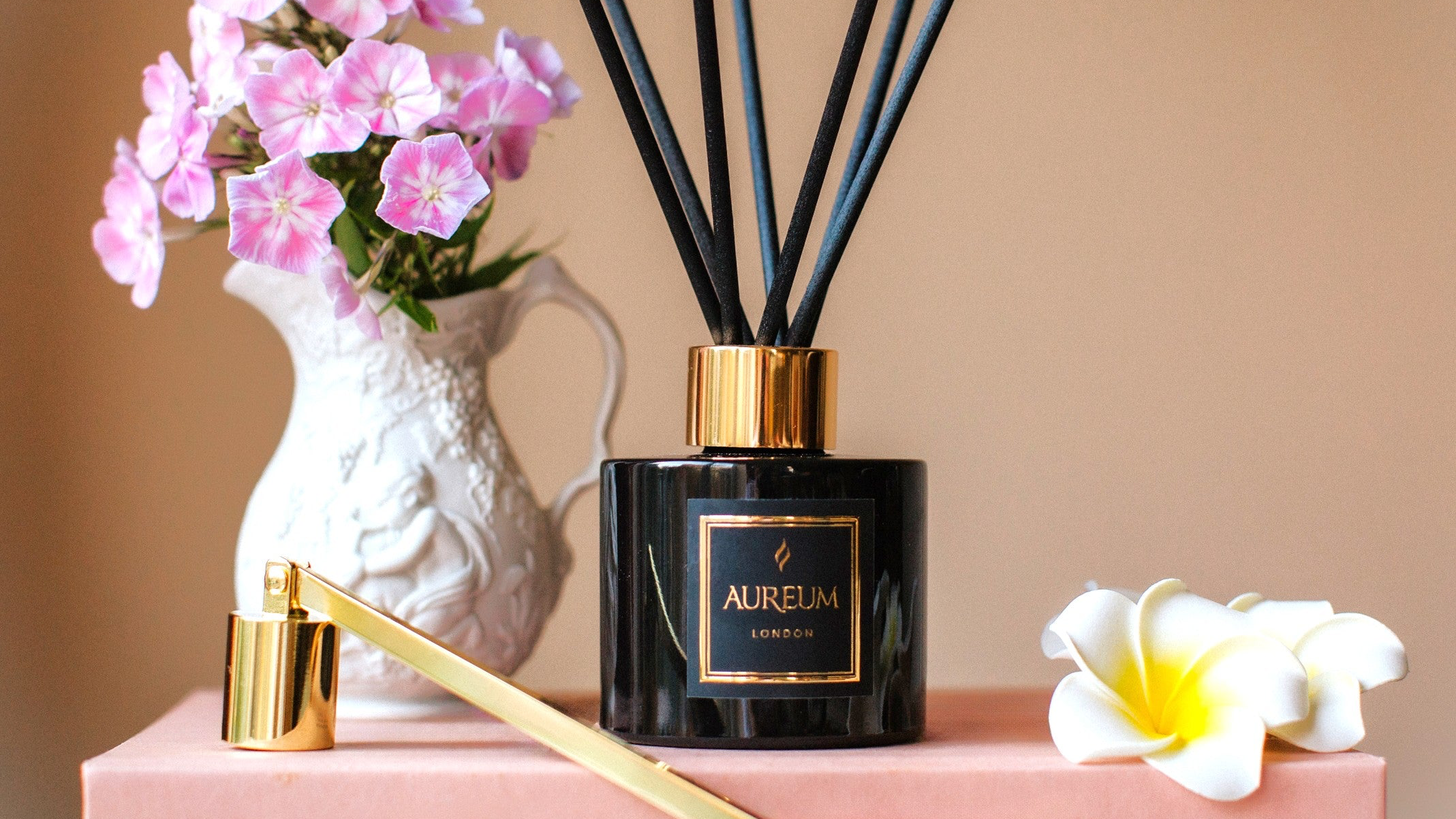 Aromatherapy diffuser with black sticks, pink flowers, and a white vase on a beige background